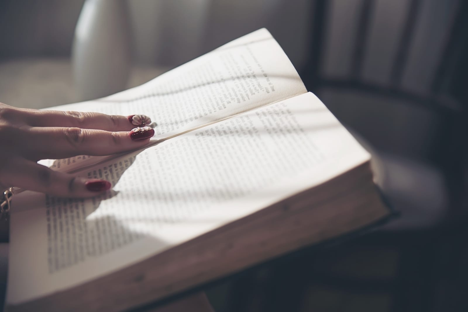 Mãos folheando as páginas de um livro aberto apoiado em uma mesa de madeira, sob luz natural