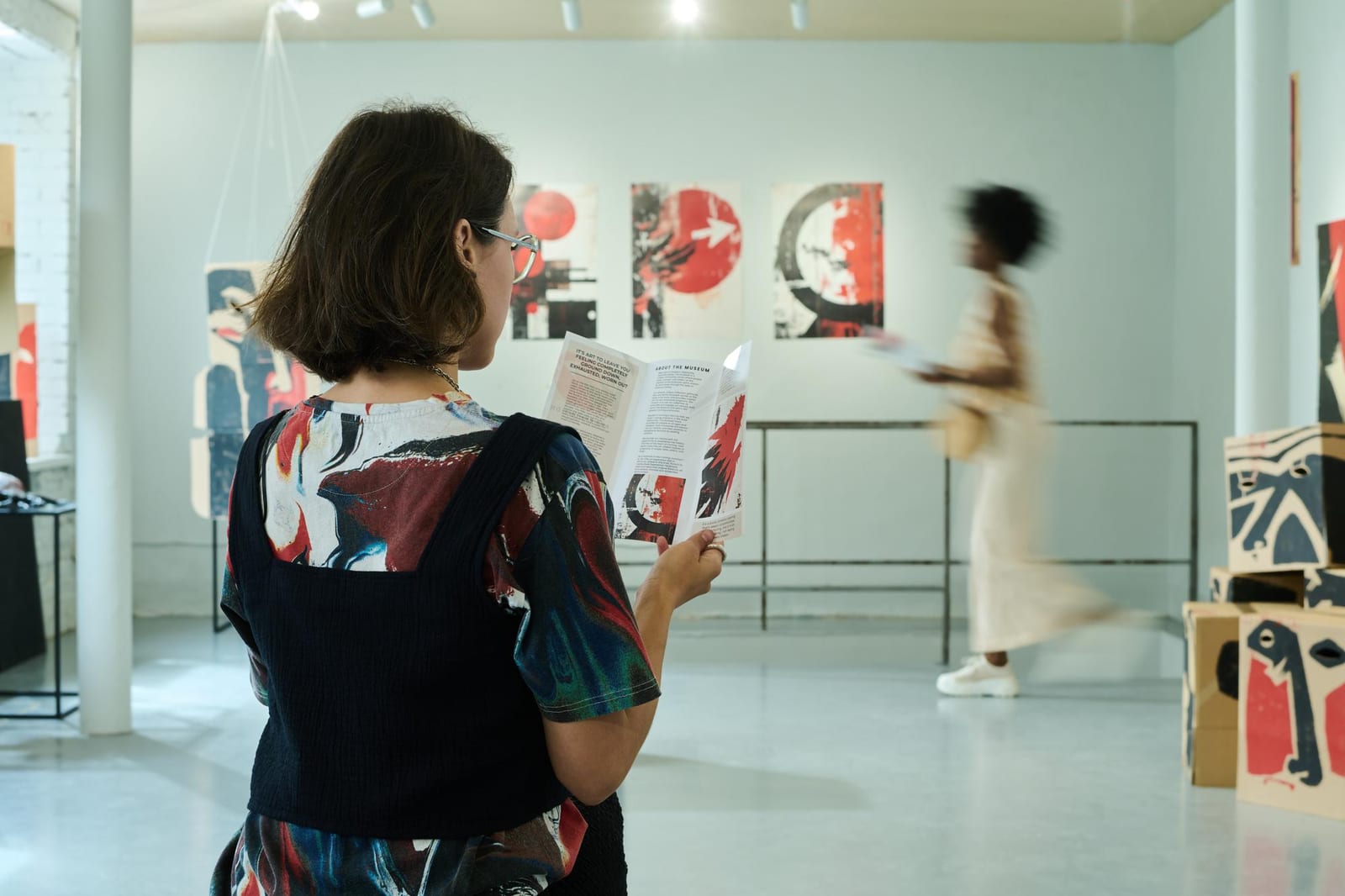 Leitora acompanha um folheto impresso enquanto caminha por um espaço de exposição